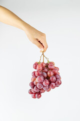 A hand on a white background is holding a bunch of fresh grapes