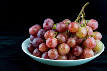 A bunch of grapes on a white plate against a black background