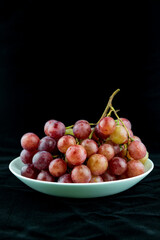 A bunch of grapes on a white plate against a black background
