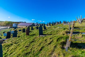 Obraz premium A view past gravestone on the hillside above the beach at the seaside resort of Aberdaron, Wales in springtime 