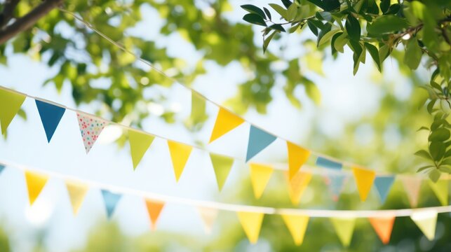 A colorful bunting banner with various colored triangular flags hanging from a tree branch against a blurred green background.
