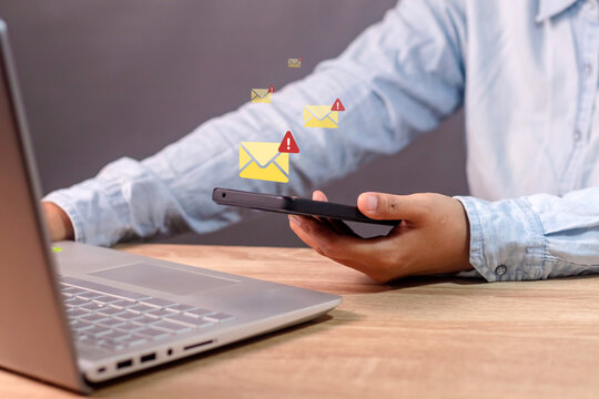 A business woman receives a malicious message on her smartphone. Email or message notification with warning symbol on smartphone.