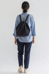 Rear view of woman in blue shirt with black drawstring backpack. Minimalist urban fashion.
