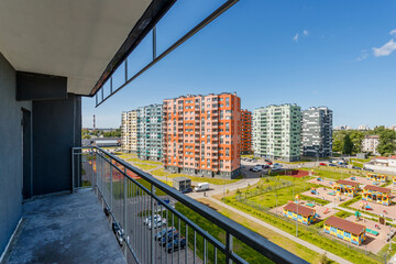 Bright multi-story buildings of a new residential complex are visible from a balcony on a sunny day. Urban landscape.