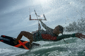 Kitesurfer performing trick on ocean wave with water splash..