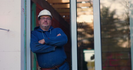 Construction worker standing with arms crossed, wearing hard hat and glasses, confident expression, construction project in progress, overseeing building site
