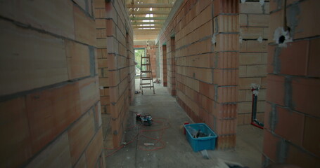 Interior view of unfinished house under construction, showing exposed brick walls, wooden framework, and a ladder in hallway