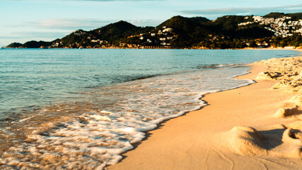  Gentle sunlight illuminates the golden sand and small waves lapping the shore. In the background