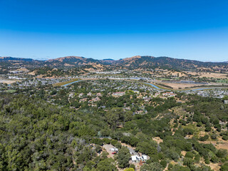 Obraz premium Aerial photos of a forested hillside in San Rafael, California, highlighting dense tree coverage, winding roads, and panoramic views of surrounding hills, residential properties, and the San Pablo Bay