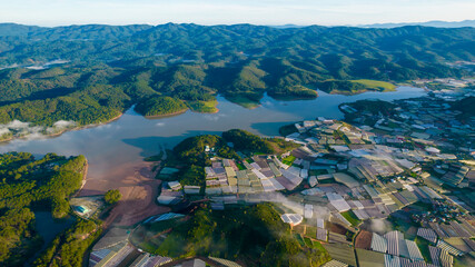 An aerial view of Dalat's Suoi Vang Lake, featuring surrounding green mountains, and extensive patterns of agricultural greenhouses.
