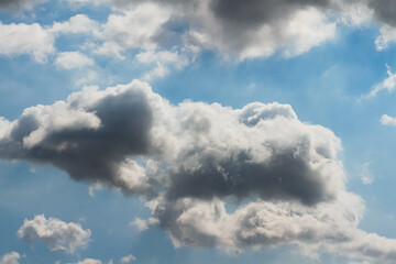 The sun hidden behind a mass of dark grey clouds, with rays of light and shadows on blue sky, for background