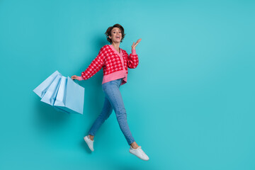Full length photo of positive excited lady wear pink cardigan holding shoppers walking emtpy space isolated teal color background