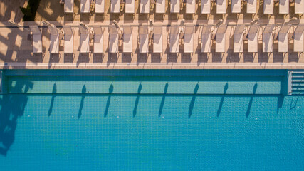 Aerial View of Empty Poolside Lounge Chairs and Blue Swimming Pool at Luxury Resort. Summer Vacation, Relaxation, and Travel Background