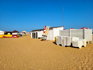 An urban seaside beach with canopies and assembled white deck chairs against a cloudless sky