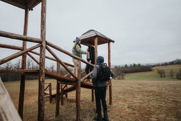 A group of friends gathering on a wooden structure in the middle of nature, enjoying each other's...