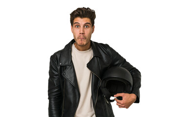 Young caucasian man holding a motrbike black helmet isolated shrugs shoulders and open eyes...