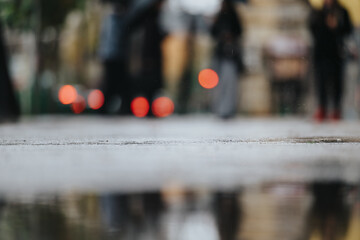 An artistic low-angle view of a wet sidewalk on a rainy day, displaying bokeh reflections and...