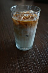 Iced latte served in a clear glass, showcasing beautiful layers of rich espresso and creamy milk over ice. Captured on a rustic wooden table, perfect for coffee and beverage themes.