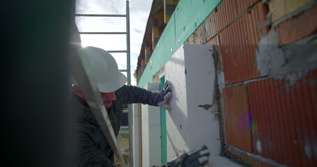 Pressing insulation panel against brick wall, construction worker aligning insulation with safety...