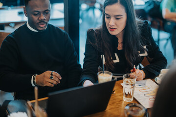 Two professionals are seen collaborating in a cafe, discussing ideas and strategies while working seamlessly on a laptop. The atmosphere is casual yet productive, fostering creativity and teamwork.