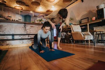 A dedicated coach assists a woman practicing yoga poses at home, promoting mindfulness, fitness,...