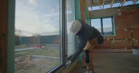 Residential construction quality check, worker in hard hat inspects window installation for...