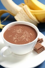 Tasty chocolate milk in cup, pieces and bananas on table, closeup