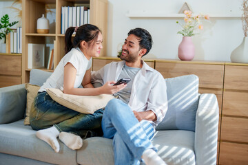 Obraz premium Couple enjoying cozy moment together on sofa, sharing smiles and laughter while looking at smartphone. warm, inviting living room features modern decor and natural light