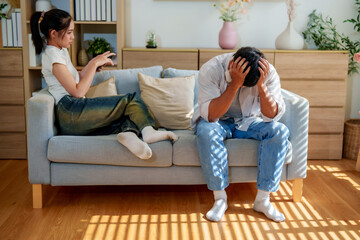 Couple sits couch, displaying emotional tension. woman appears disengaged, using her phone, while...