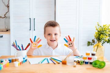 a small child draws with pencils or paints at home at a table in a bright room or art school, a...