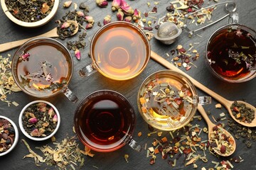 Different herbal teas and dry leaves on black table, flat lay