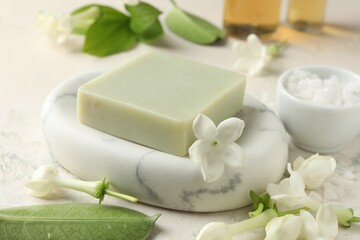 Bar of soap, sea salt and jasmine flowers on light table, closeup