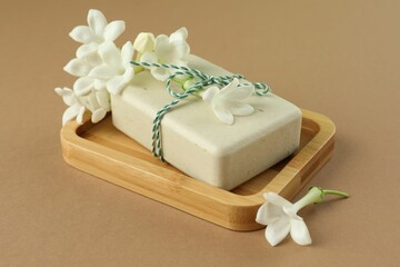 Bar of soap and jasmine flowers on light brown background, closeup
