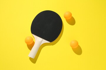 Ping pong racket and balls on yellow background, top view