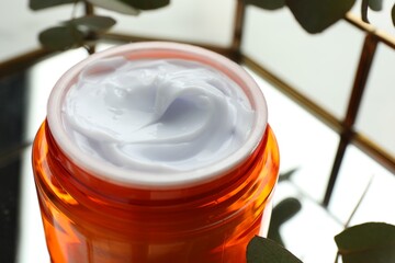 Fototapeta na wymiar Jar of moisturizing body cream, leaves and glass tray on white table, closeup