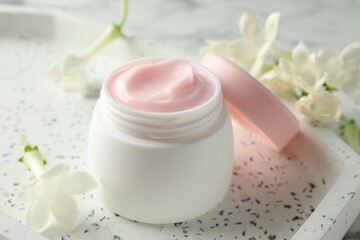 Jar of moisturizing body cream and flowers on white table, closeup