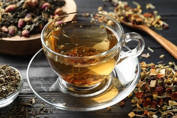 Refreshing herbal tea and dry leaves on black wooden table, closeup
