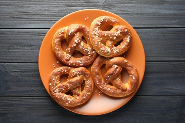 Tasty pretzels with salt on dark wooden table, top view