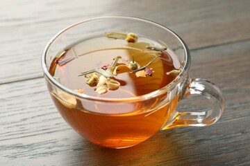 Aromatic herbal tea in glass cup on wooden table, closeup