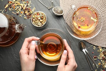Woman with aromatic herbal tea at black table, top view