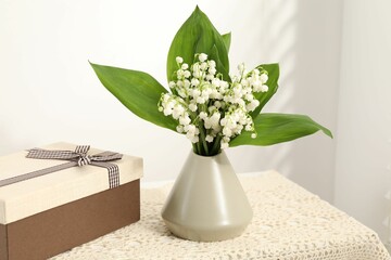 Beautiful lilies of the valley flowers and gift on table