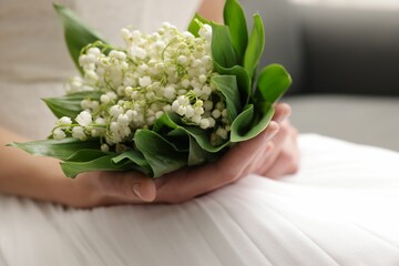 Bride with bouquet of beautiful lilies of the valley on sofa indoors, closeup