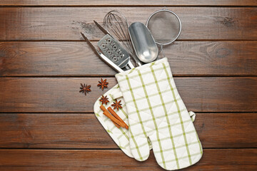 Different kitchen utensils in oven mitten, cinnamon and anise stars on wooden table, flat lay