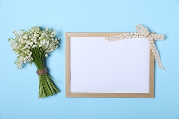 Beautiful lily-of-the-valley flowers and blank frame on light blue background, top view. Space for text
