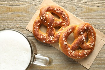 Tasty pretzels and glass mug of beer on wooden table, flat lay