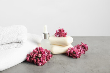 Stack of soap bars, essential oil, towels and lilac flowers on grey textured table against light background, closeup