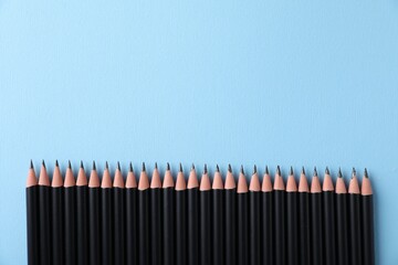 Many sharp graphite pencils on light blue background, flat lay. Space for text