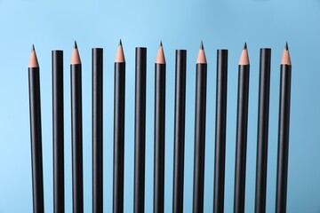 Many sharp graphite pencils on light blue background, closeup