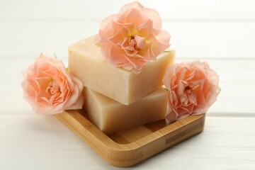 Soap bars and beautiful flowers on white wooden table, closeup