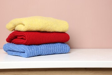 Stack of woolen sweaters on white table against color background. Space for text